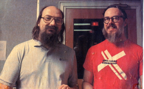 Photo of two white, bearded men. They are both wearing thick glasses. The person on the left is wearing gray-blue polo shirt. The person on the right is wearing a red tshift with big X and Bell Labs Sensitive text in center